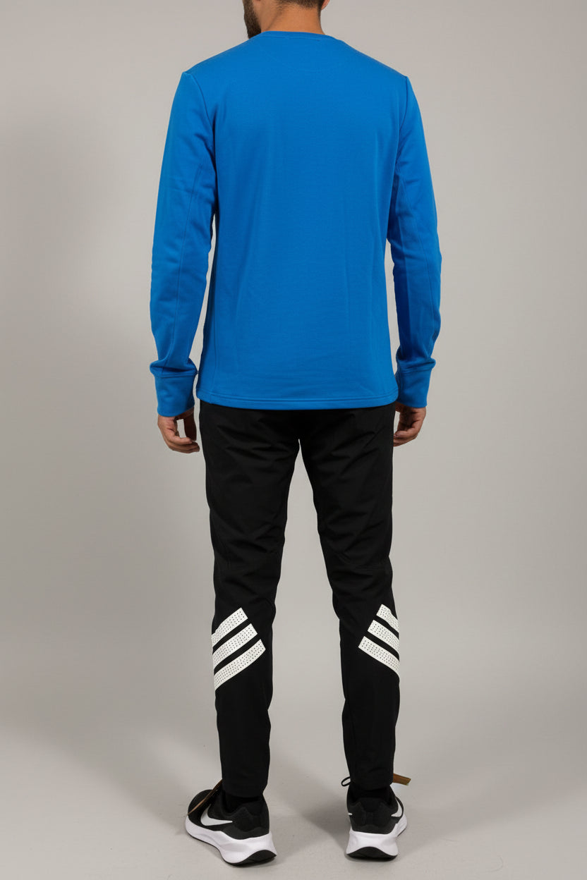 Person wearing a blue hoodie and black pants with white stripes, standing against a plain wall.