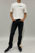 Person wearing a white t-shirt and black pants standing against a white wall.