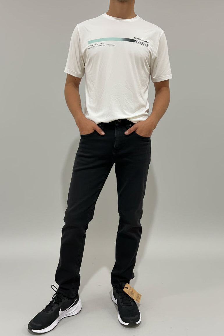 Person wearing a white t-shirt and black pants standing against a white wall.