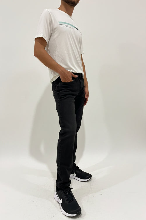 Person wearing a white t-shirt, black pants, and black sneakers against a plain wall.